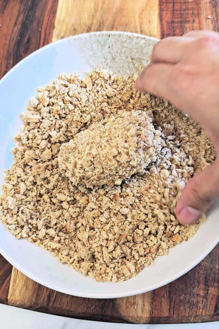 Coating a chicken croquette in panko breadcrumbs.
