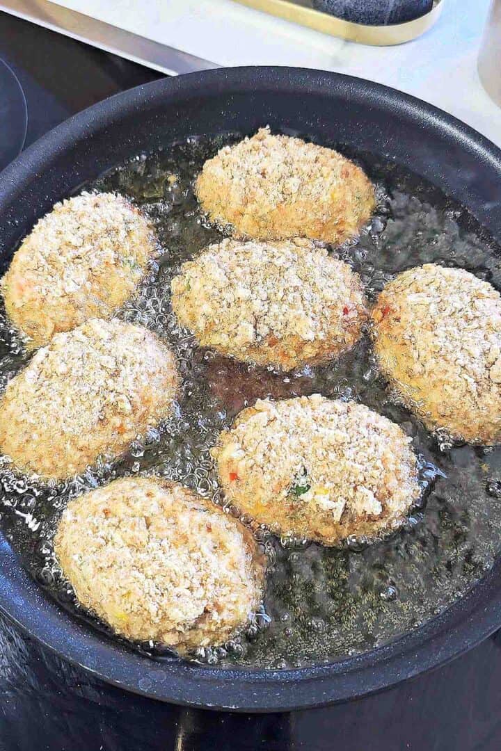 Chicken croquettes frying in a skillet.