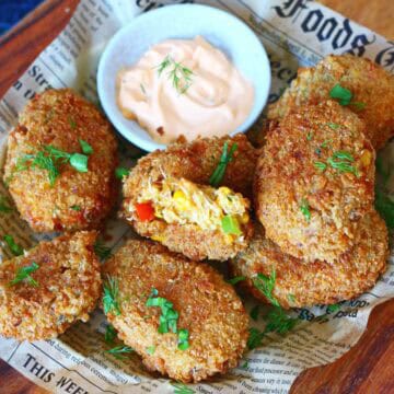 Overhead view of cheesy chicken croquettes with vegetables arranged on newspaper paper with a dipping sauce in the center.