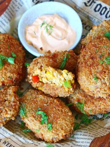 Overhead view of cheesy chicken croquettes with vegetables arranged on newspaper paper with a dipping sauce in the center.