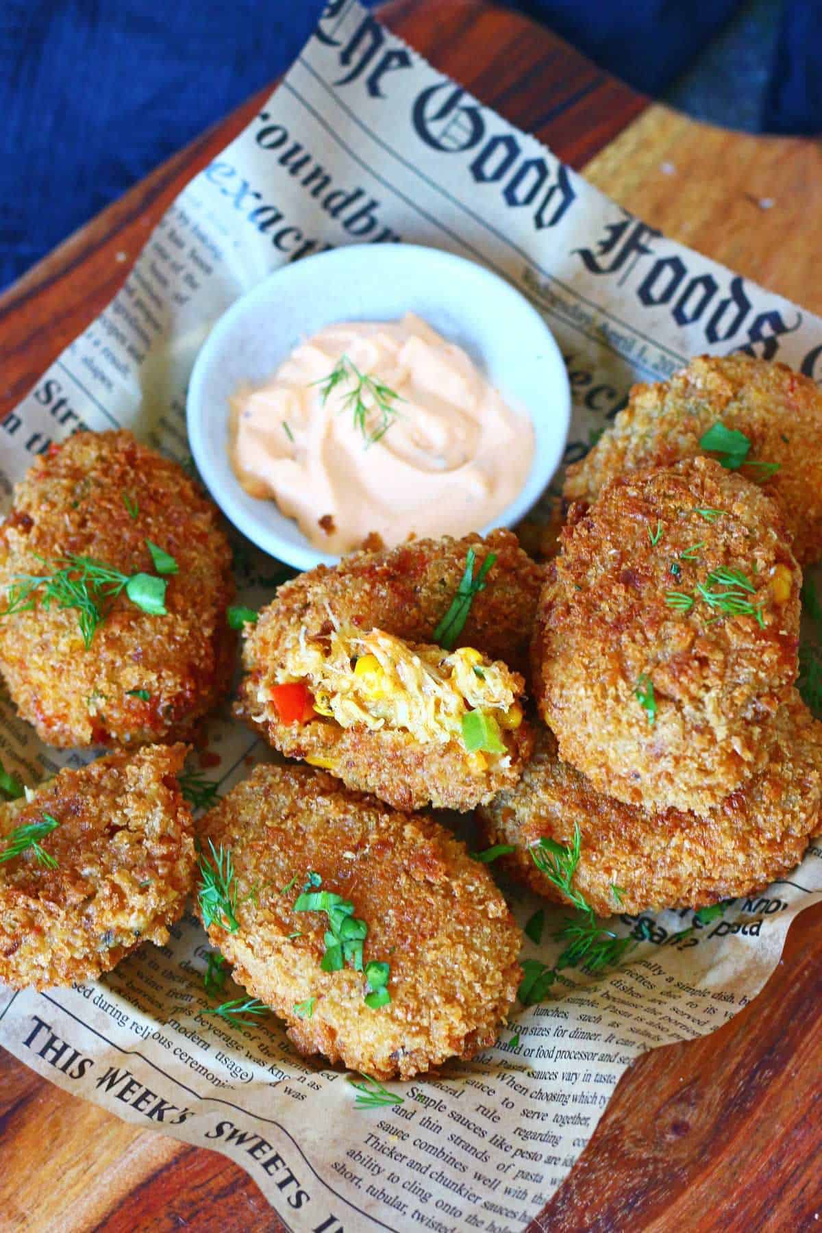 Cheesy chicken vegetable croquettes on a wooden board lined with newspaper paper, one broken open to reveal the colorful filling.