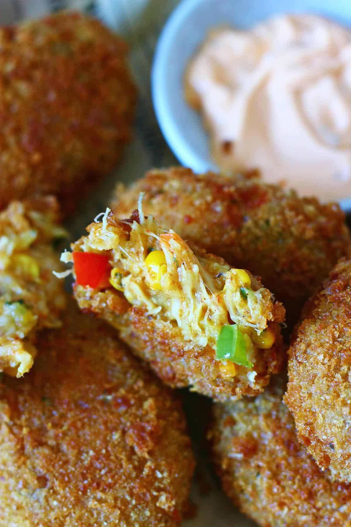Close up of a cheesy chicken croquette broken in half showing the shredded chicken, sweet corn, red and green bell pepper filling.