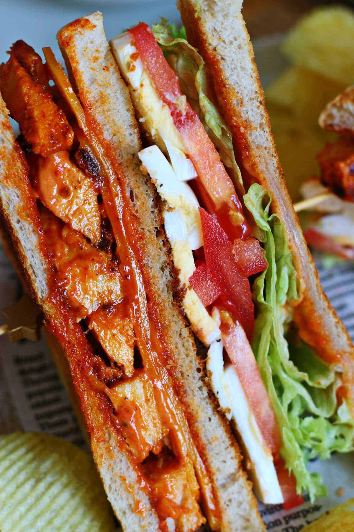 Close-up of a tandoori chicken club sandwich with crispy chips.
