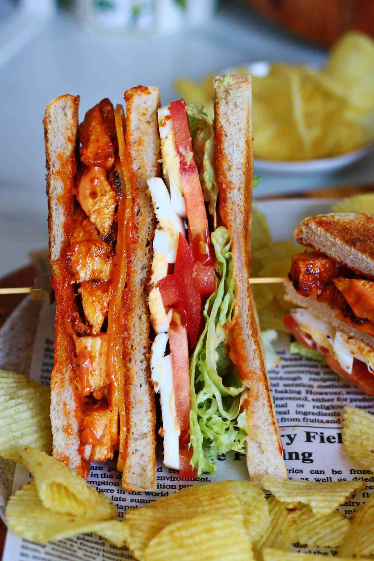 Tandoori chicken club sandwich secured with a sandwich pick and served with chips.