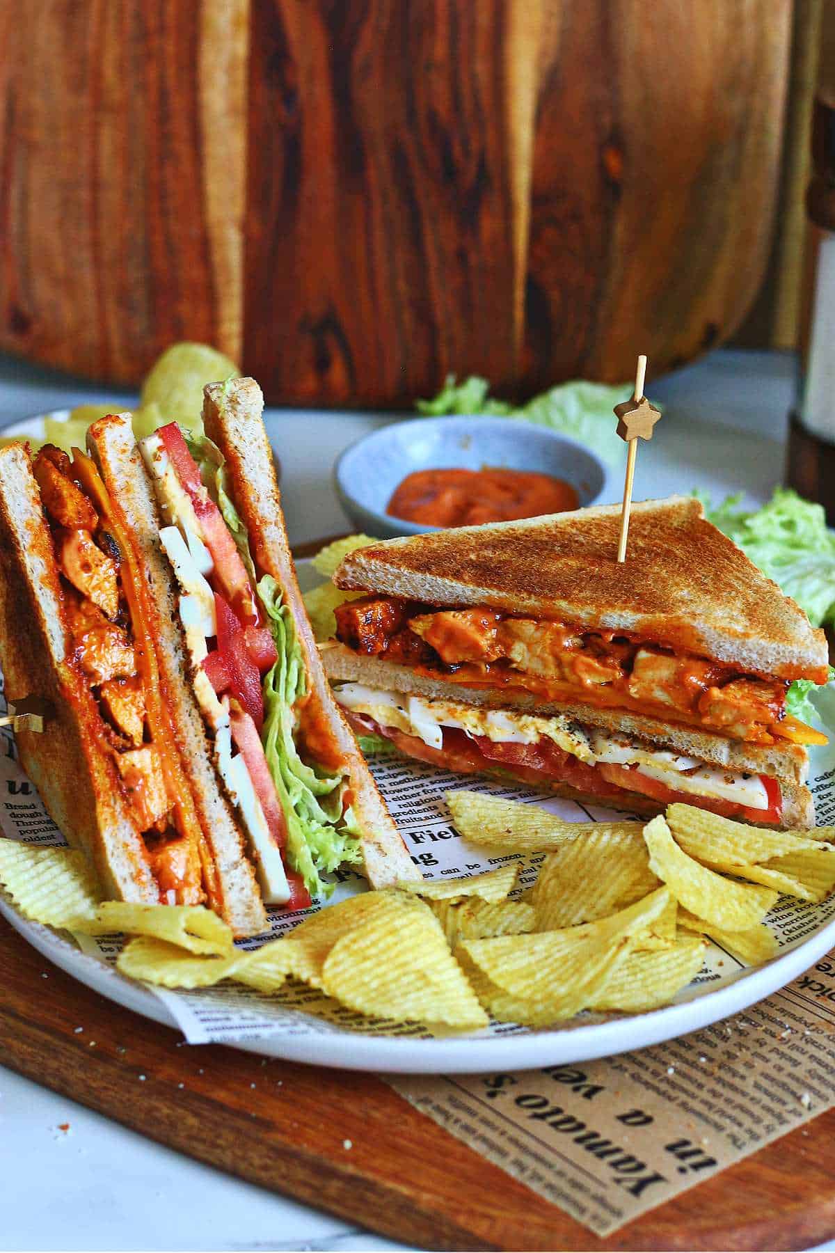 Two tandoori chicken club sandwiches served on a plate with potato chips.