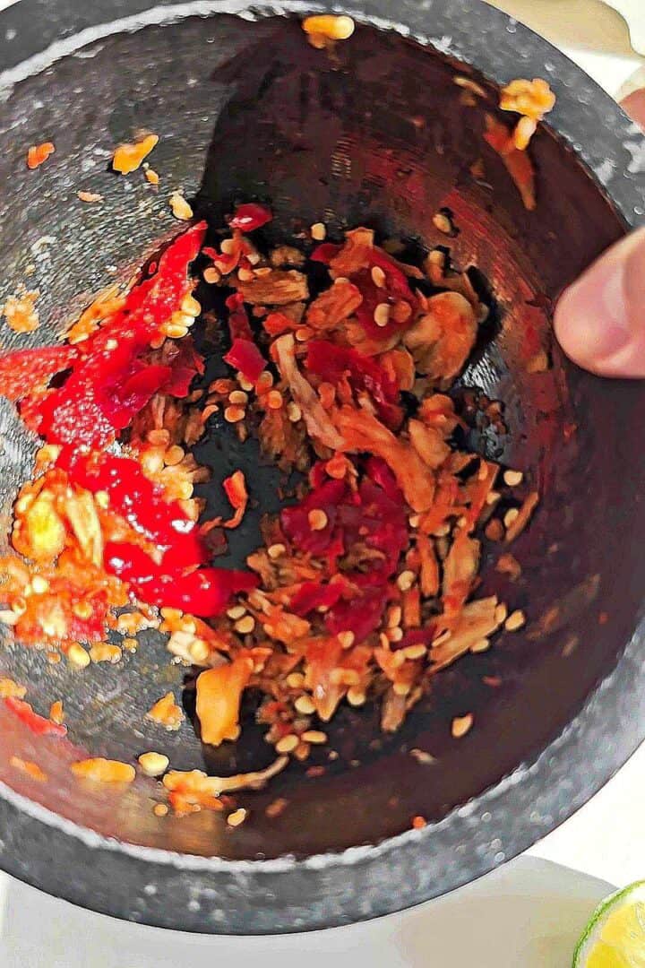 Garlic and bird's eye chilies pounded into a rough chili garlic paste in a stone mortar.