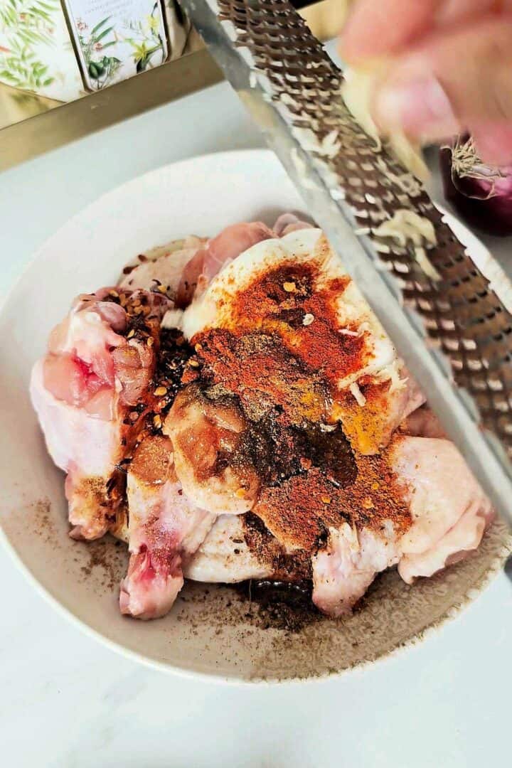 Chicken wings topped with grated garlic and tandoori spices before marinating.