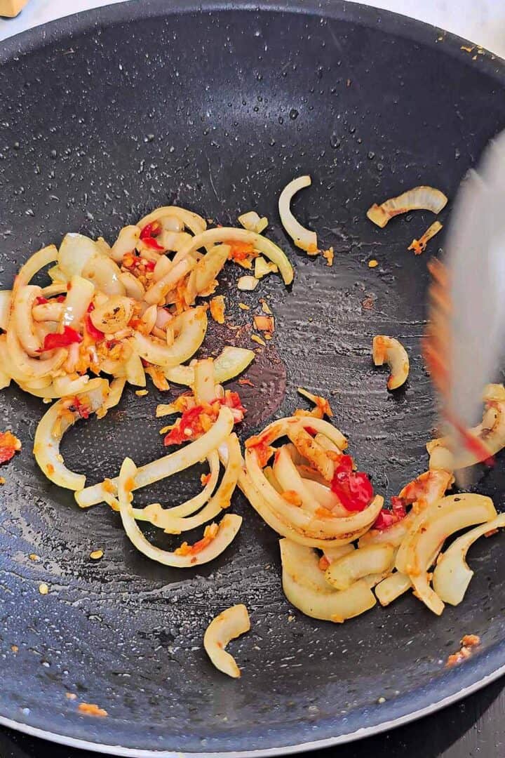 Sliced onion stir-fried with chili garlic paste in a wok.