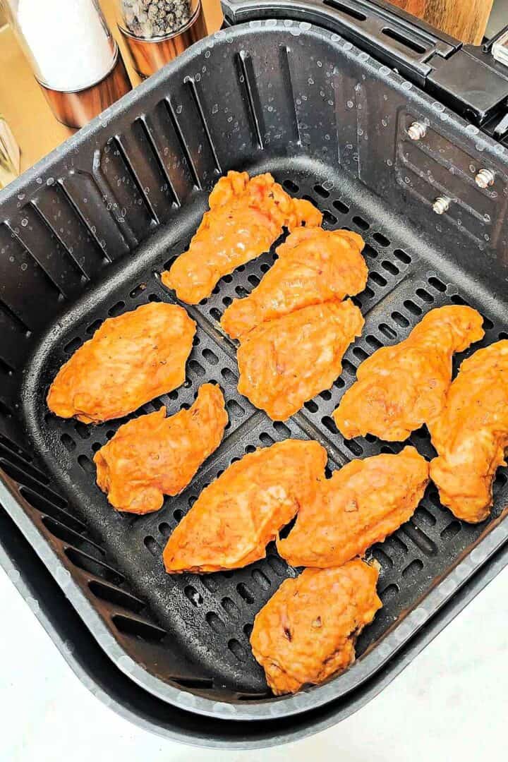 Marinated tandoori chicken wings arranged in a single layer in the air fryer basket.