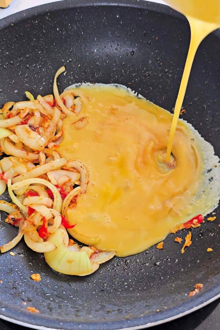 Beaten eggs poured into the wok beside the stir-fried onions.