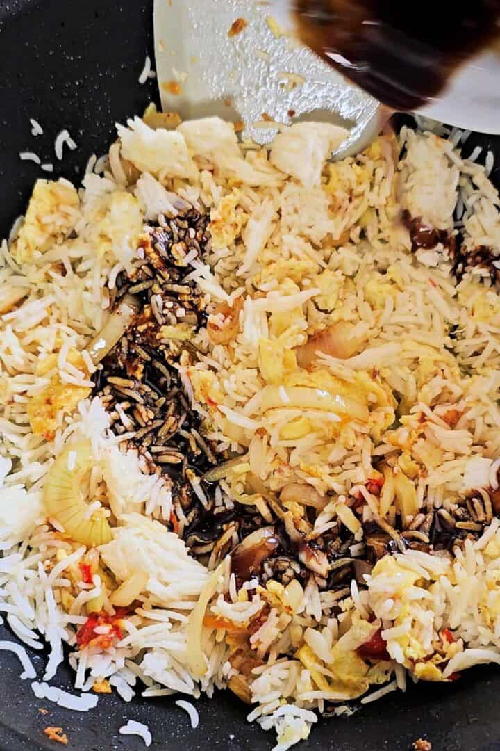 Sauce poured over cooked rice, scrambled egg, and onion in a wok.