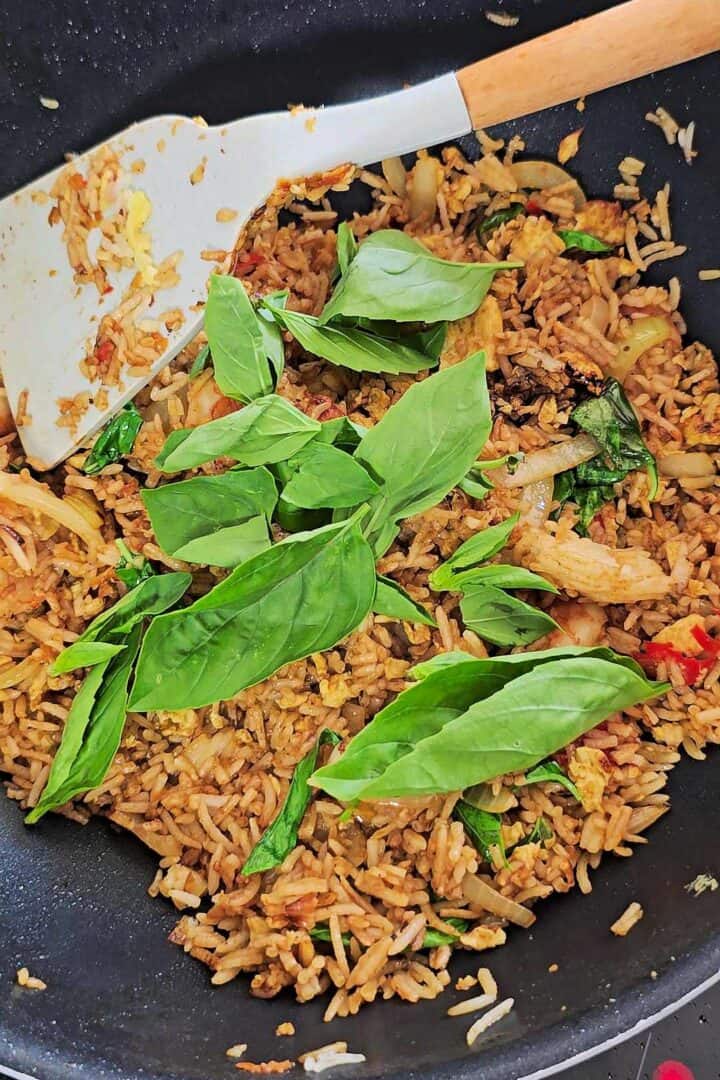 Fresh Thai basil leaves added on top of shrimp fried rice in the wok.