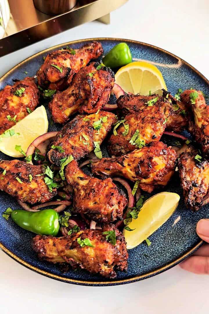 Tandoori chicken wings served on a blue plate with lemon wedges, red onion, and green chili.