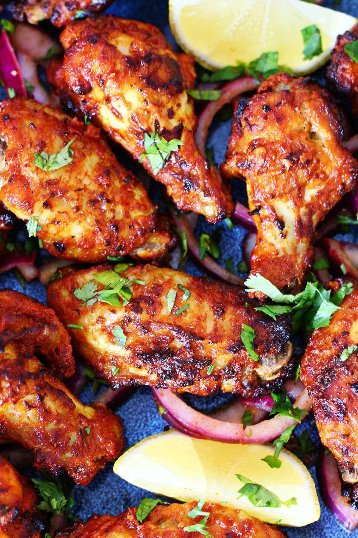 Close-up of air fryer tandoori chicken wings with charred edges, cilantro, red onion, and lemon wedges.