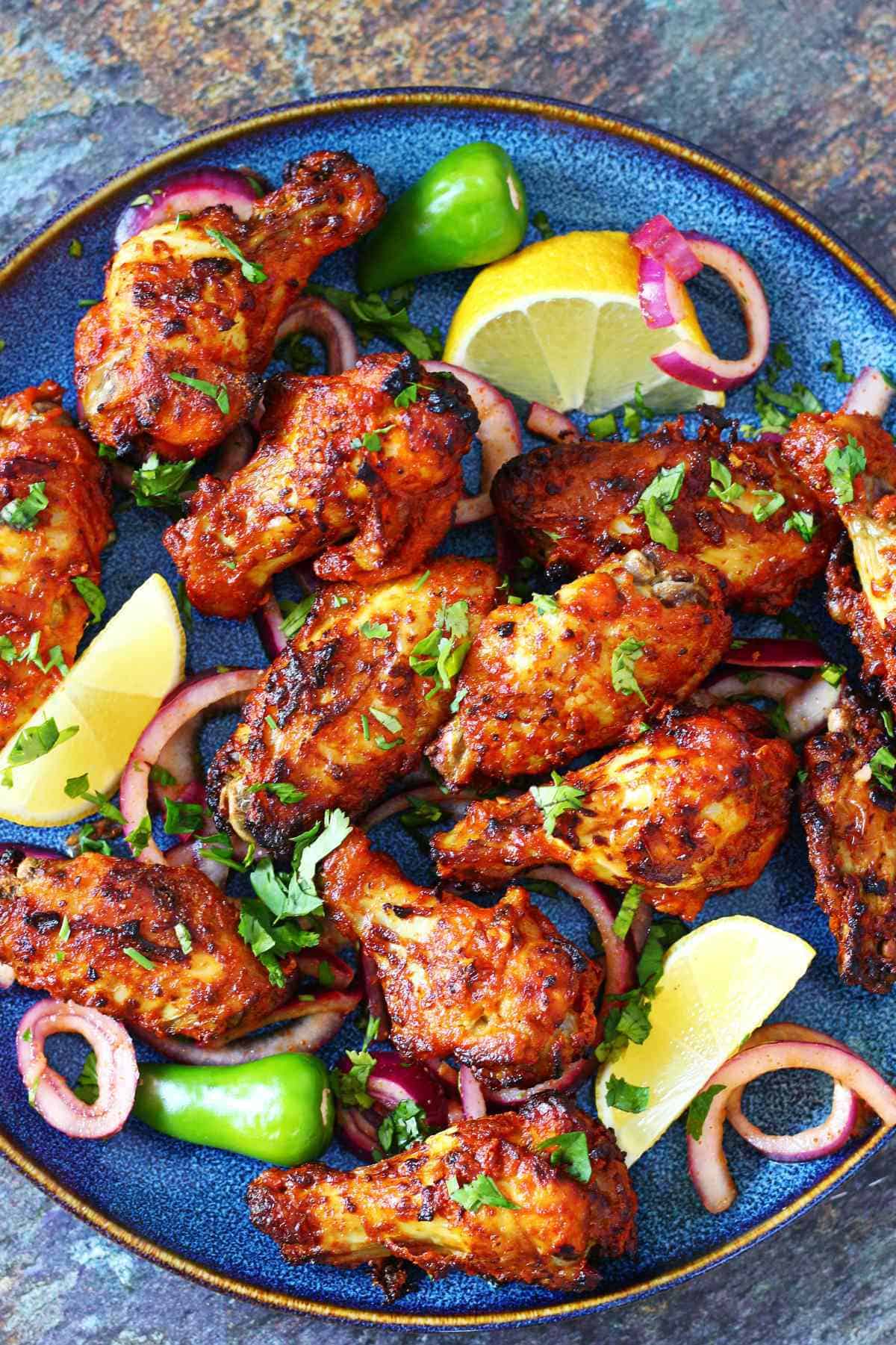 Air fryer tandoori chicken wings served on a blue plate with lemon wedges, red onion, and green chili.