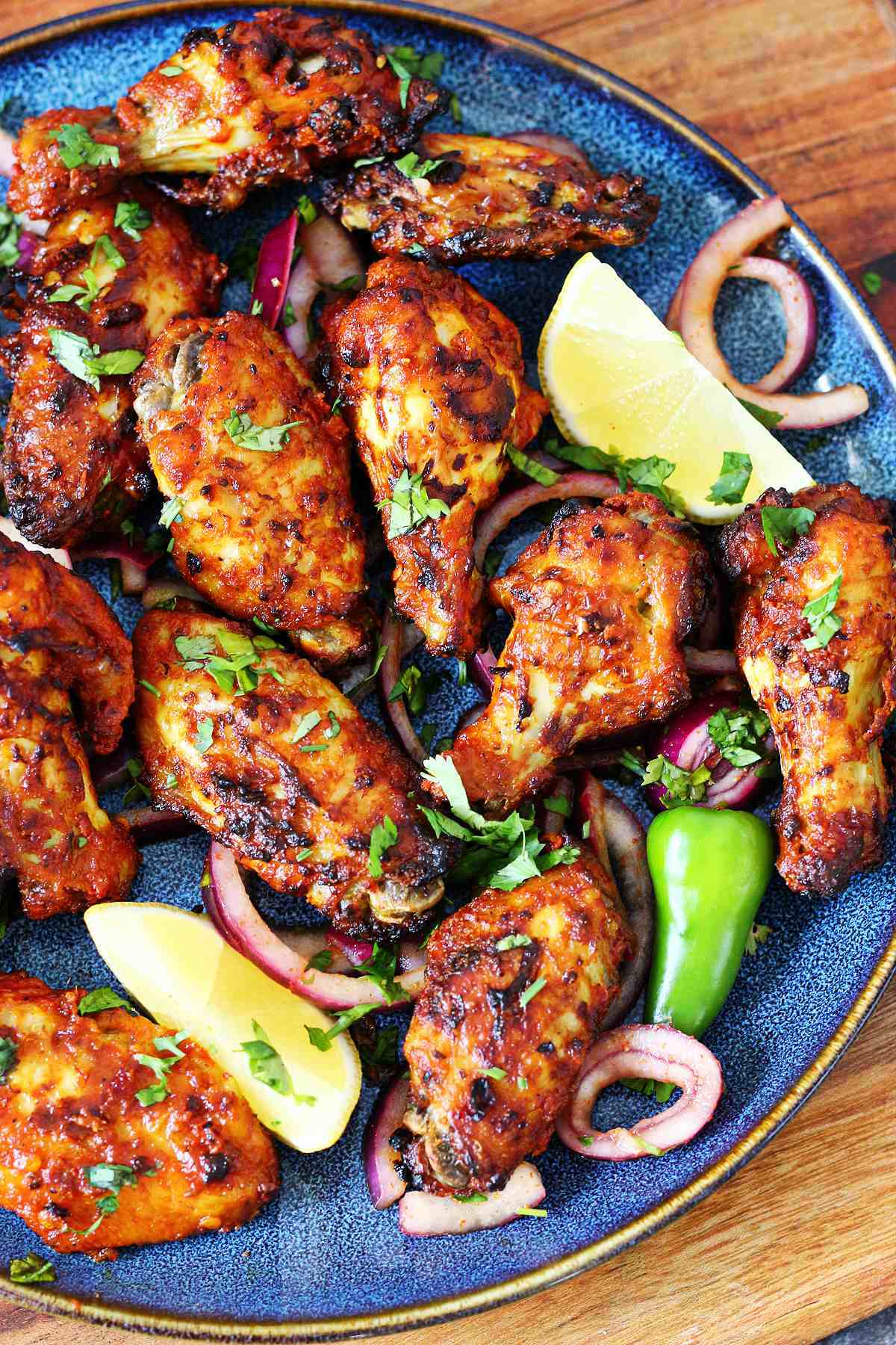 Tandoori chicken wings on a blue plate garnished with cilantro, red onion, and lemon.