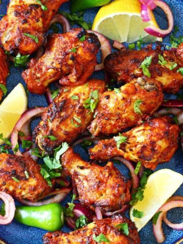 Overhead shot of tandoori chicken wings with charred skin, red onion rings, and lemon wedges.