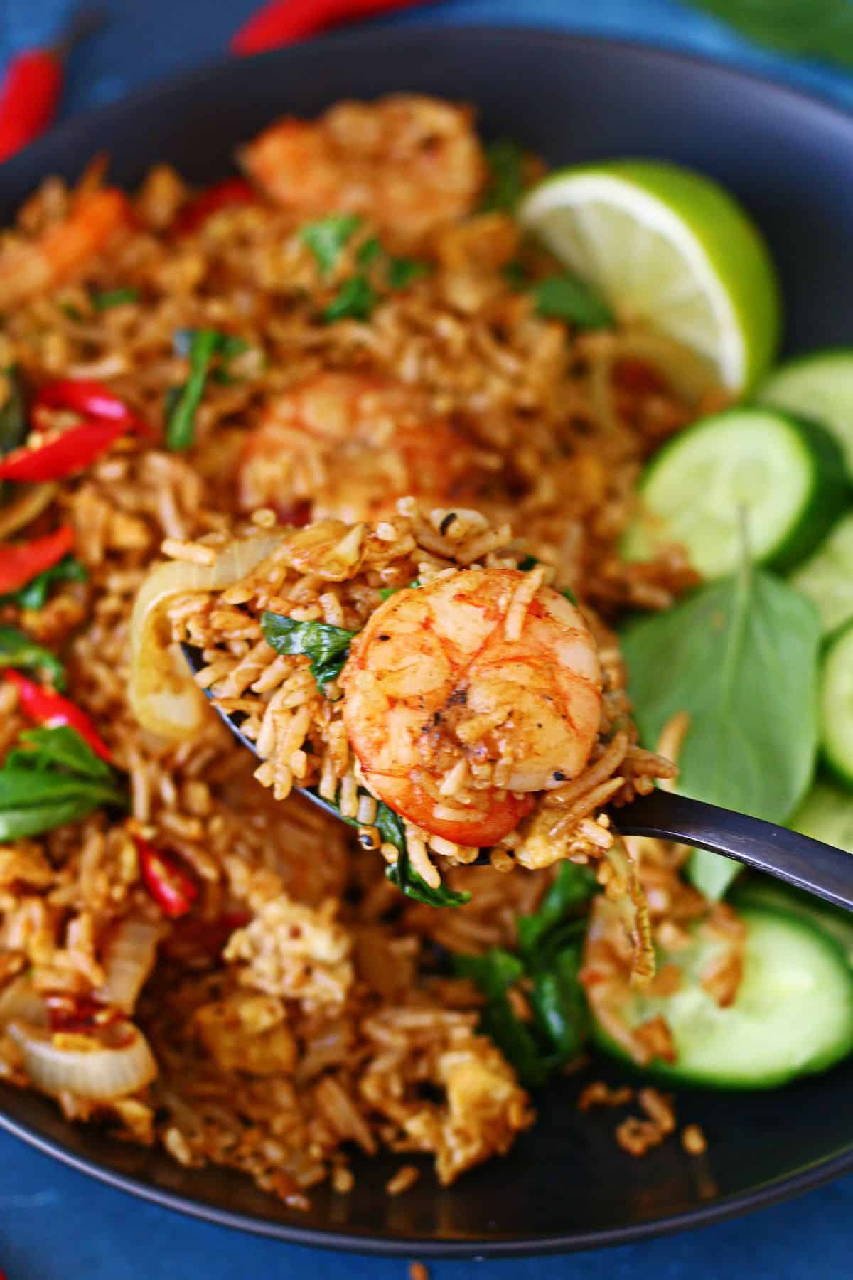 A spoonful of Thai basil shrimp fried rice with a seared shrimp, held over the bowl.