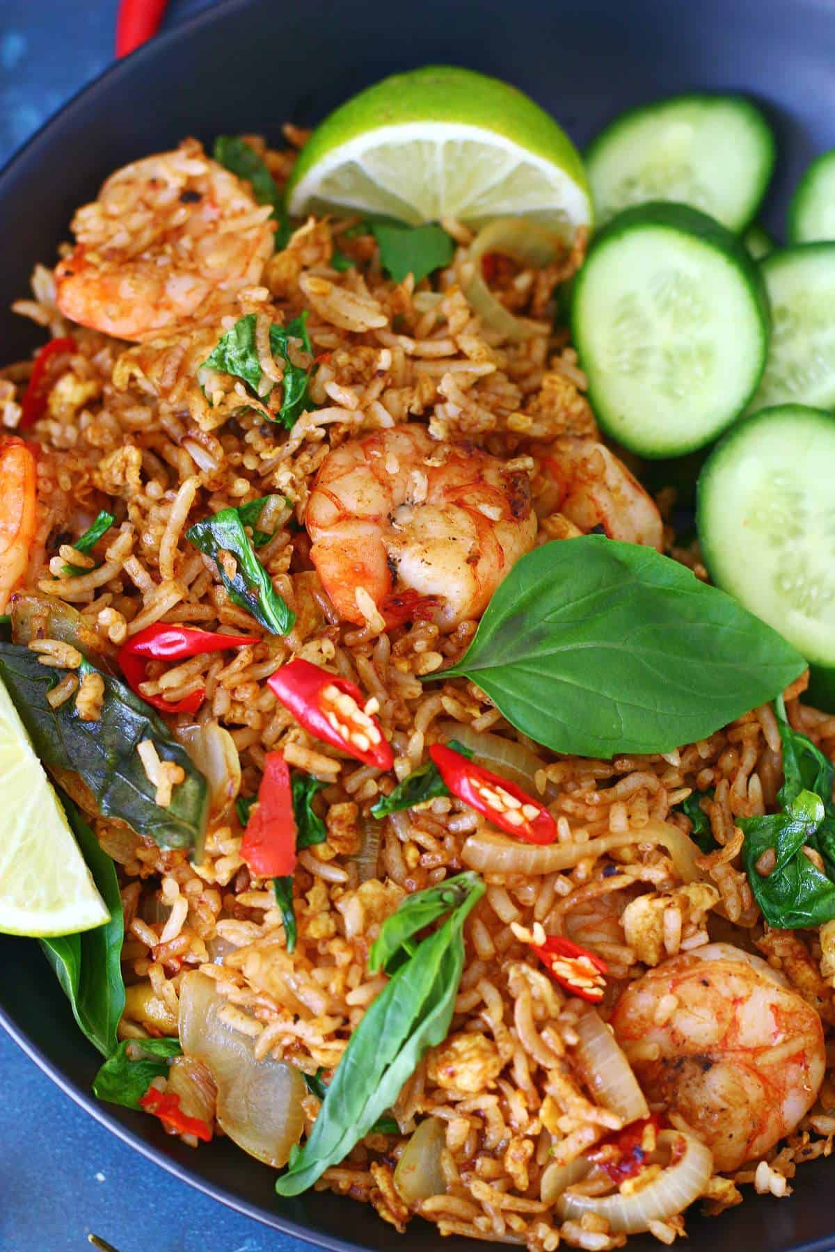 Close-up of Thai basil shrimp fried rice with seared shrimp, sliced red chilies, lime, and cucumber.