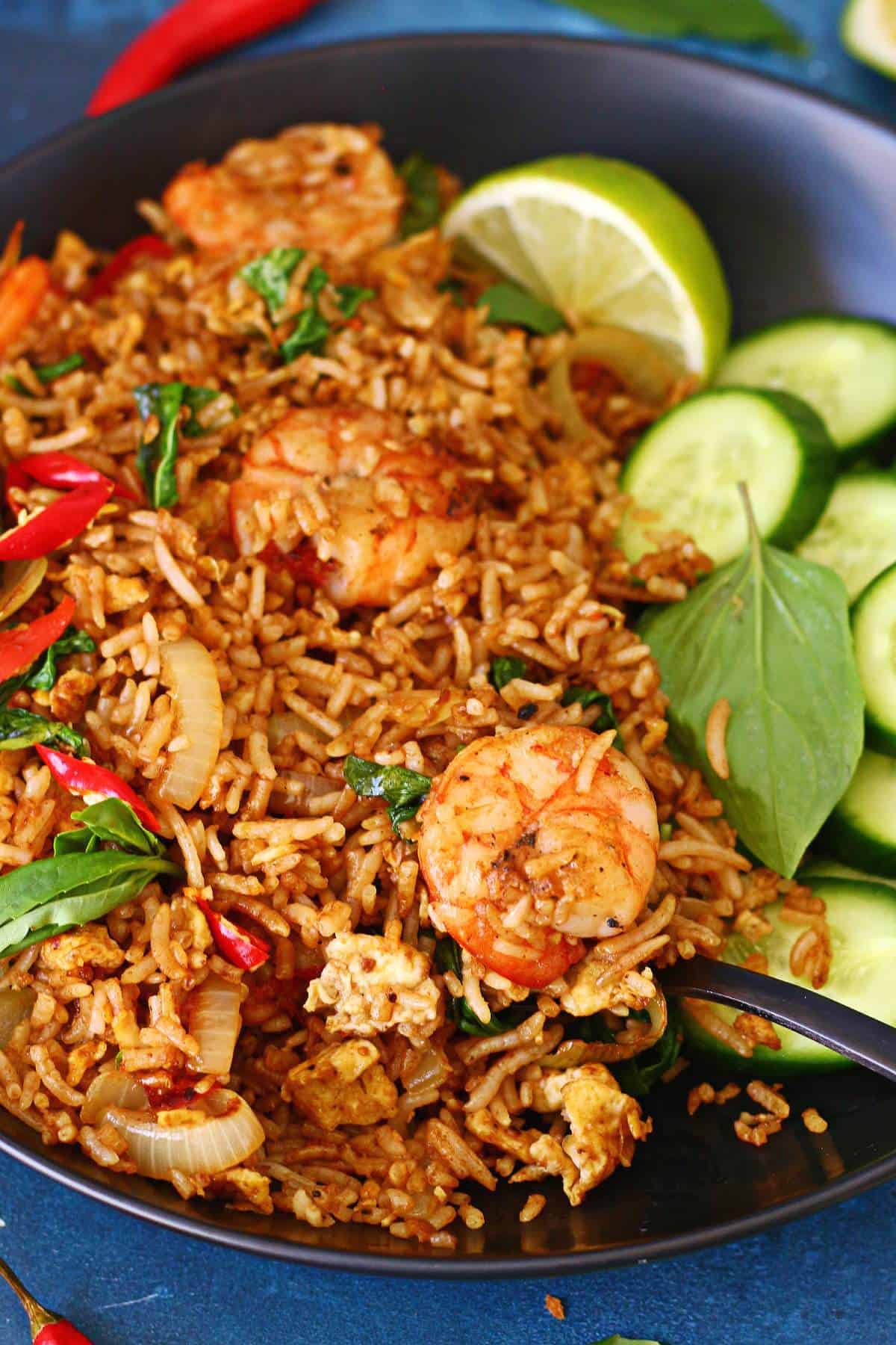 Close-up of shrimp fried rice with Thai basil, scrambled egg, and red chilies, with a fork in the bowl.