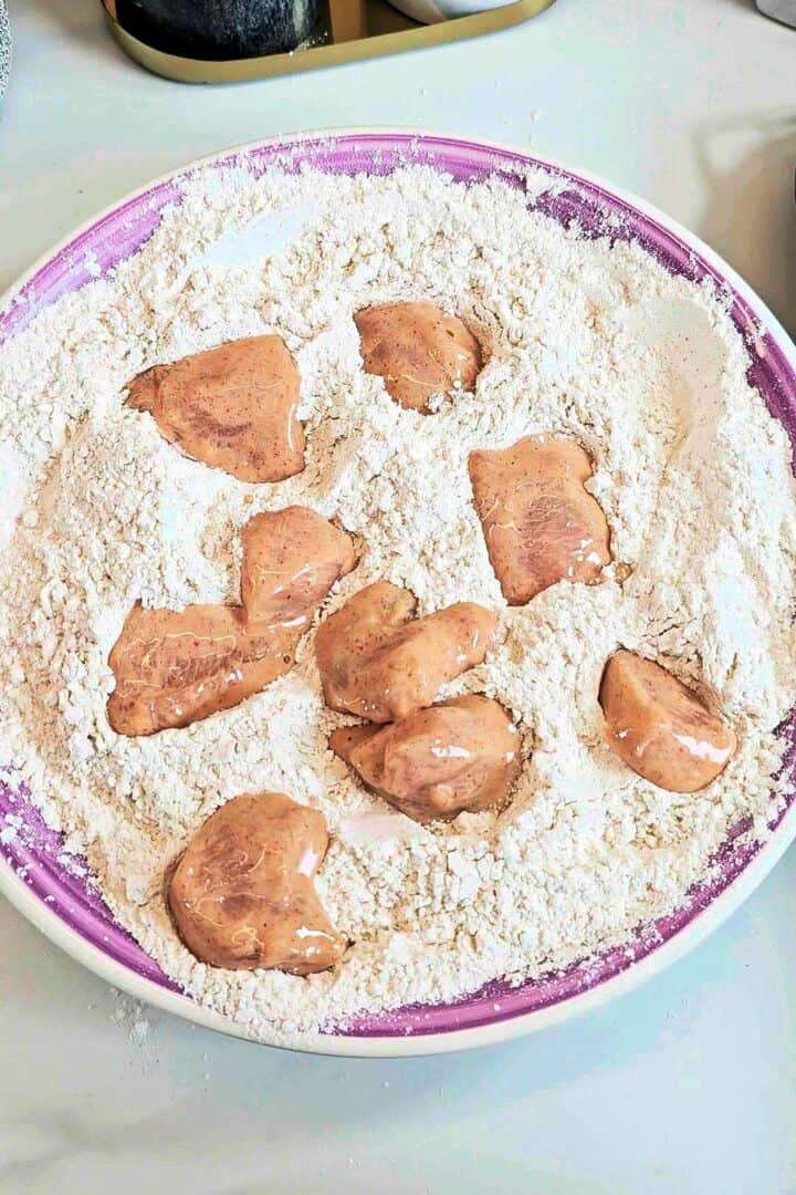 Marinated chicken pieces in a plate of seasoned flour.