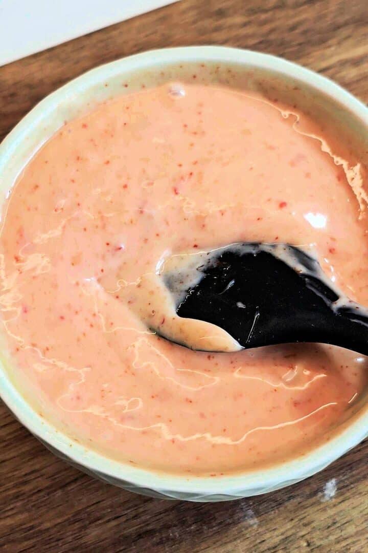Creamy bang bang sauce in a small bowl with a black spoon.