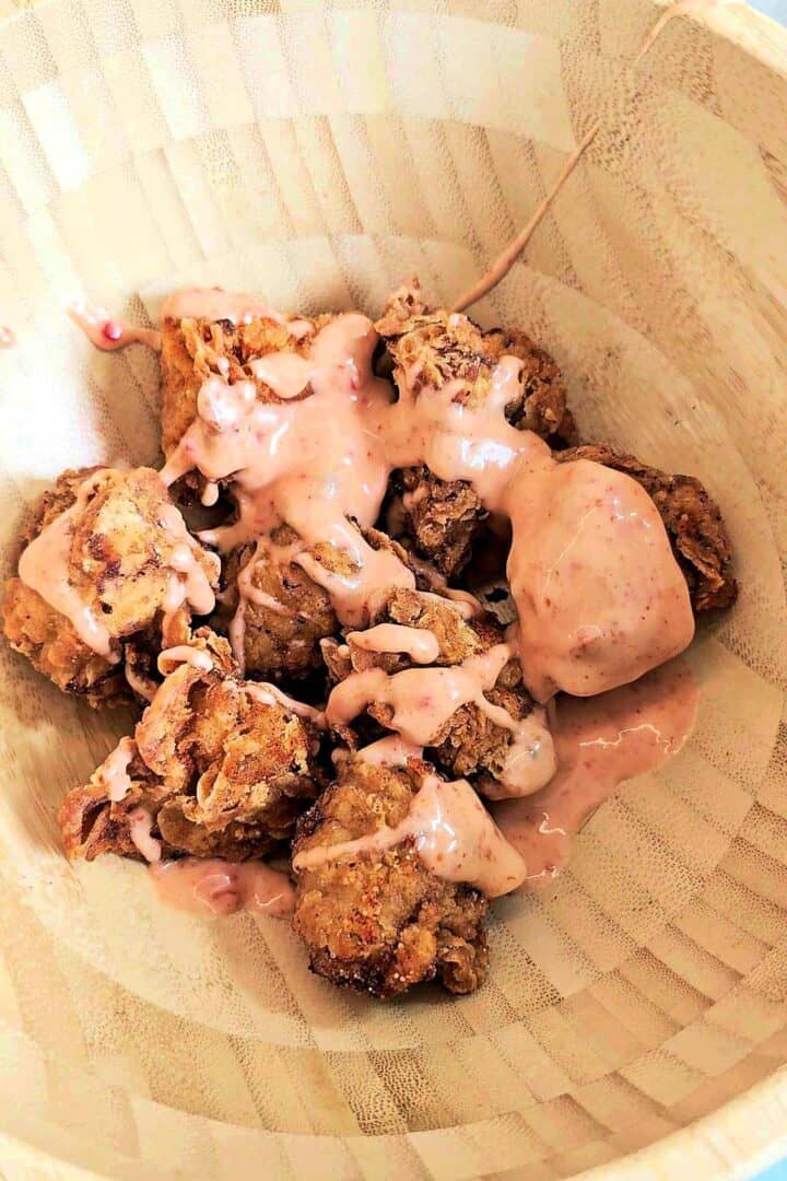 Fried chicken drizzled with bang bang sauce in a wooden bowl, ready to toss.