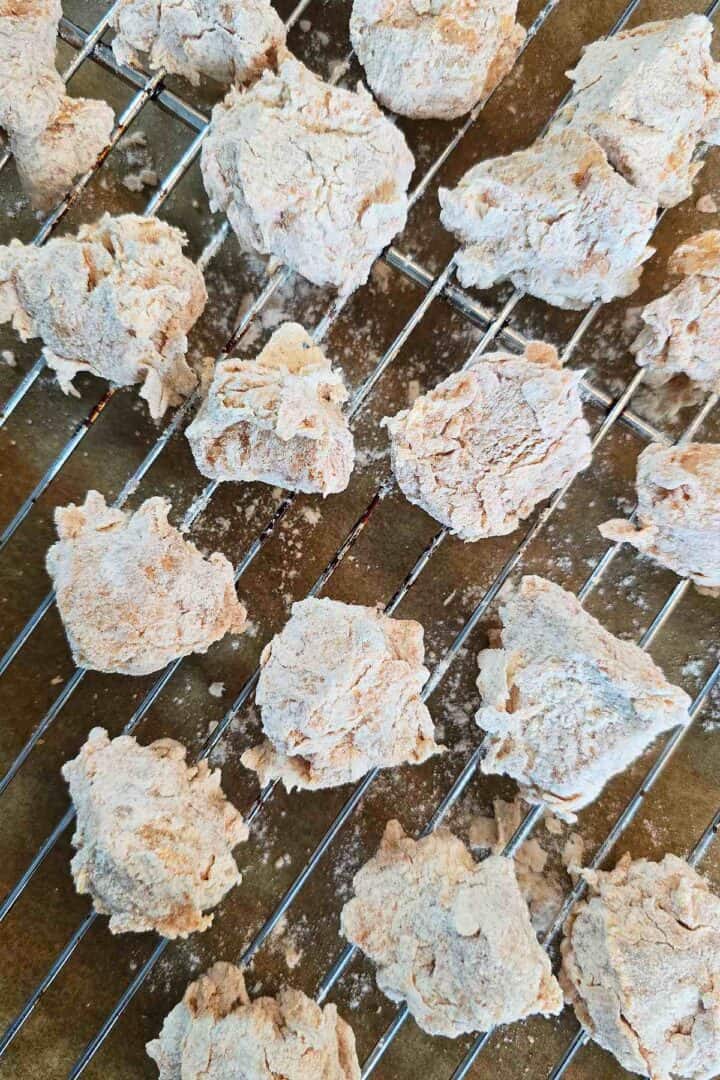 Coated raw popcorn chicken pieces resting in a single layer on a wire rack.