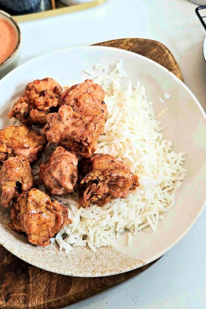 Sauce-coated fried chicken over steamed basmati rice in a white bowl.