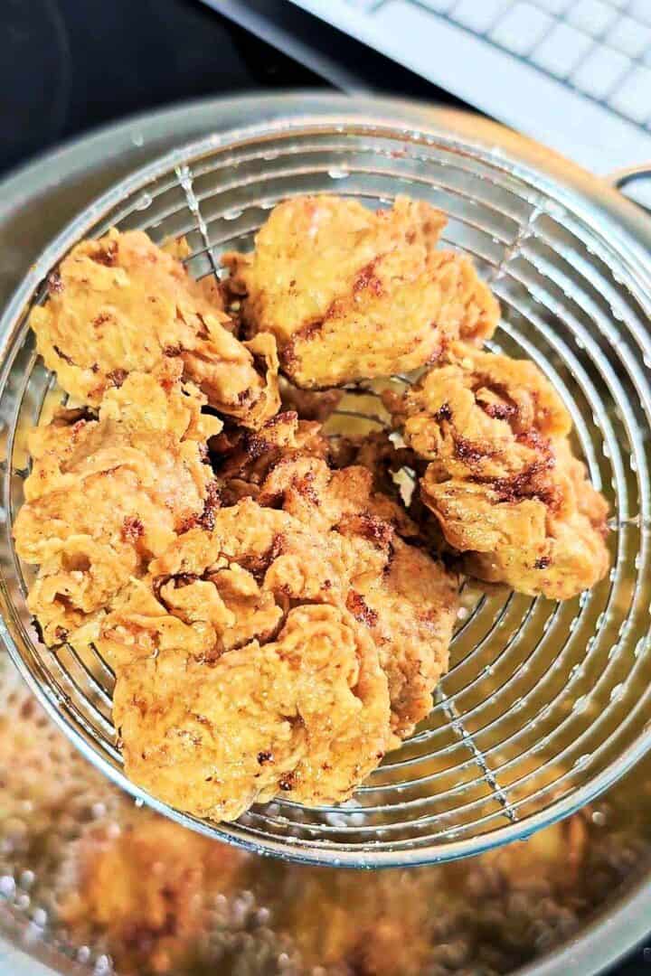 Golden fried popcorn chicken lifted out of hot oil with a spider strainer.
