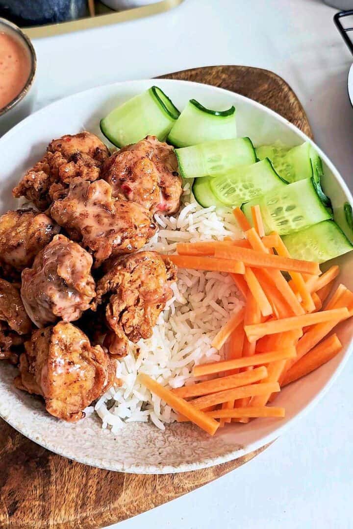 Rice bowl with saucy fried chicken, cucumber ribbons and carrot sticks.