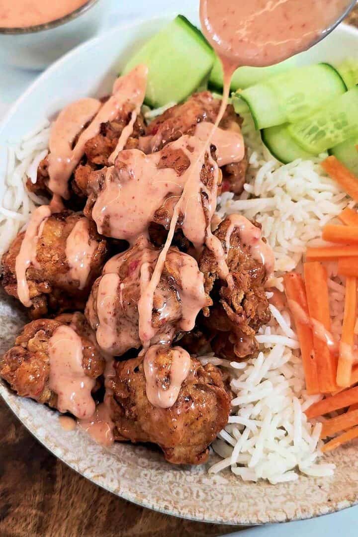 Extra sauce being drizzled from a spoon over the chicken in a bang bang chicken bowl.
