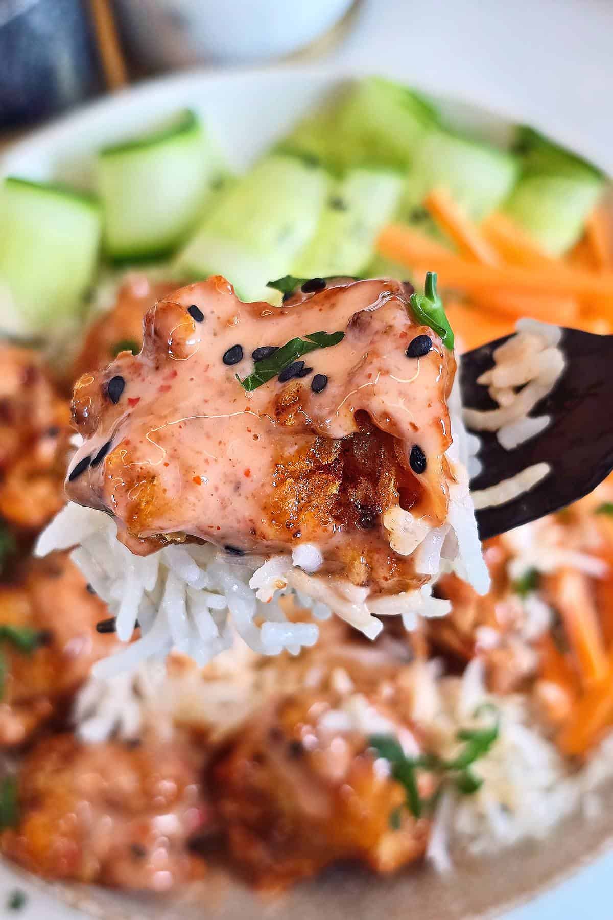 A forkful of rice and crispy chicken coated in bang bang sauce, held over the bowl.