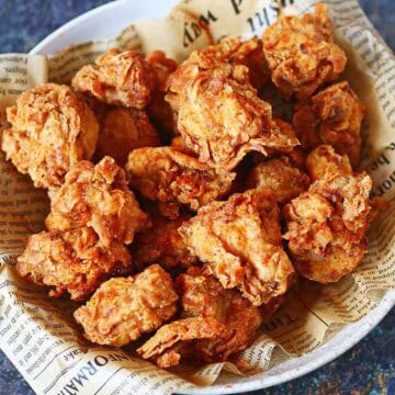 Bowl of homemade spicy popcorn chicken with a crispy, flaky coating on newspaper-lined paper.