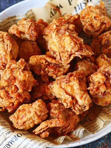 Bowl of homemade spicy popcorn chicken with a crispy, flaky coating on newspaper-lined paper.